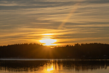 Golden sunrise over calm autumn sea with forest on the shore and gentle fog above the water, peaceful natural seascape and morning atmosphere