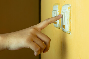 A human hand pressing a light switch on a yellow wall, symbolizing saving energy and controlling electricity at home, landscape