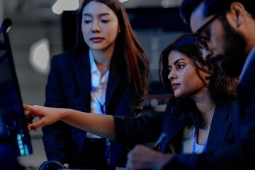 A diverse team of three professionals, one man and two women, collaborates closely around a computer screen, analyzing data and discussing project details in a modern tech office.