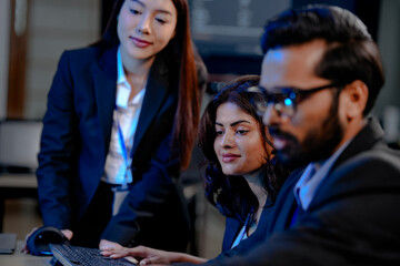 A diverse team of three professionals, one man and two women, collaborates closely around a computer screen, analyzing data and discussing project details in a modern tech office.