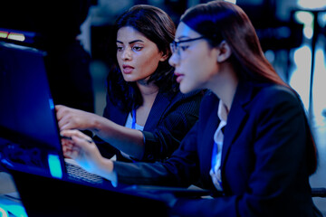 Late night code warriors: Two female developers intensely debugging code together, eyes locked on the screen, determined to solve a complex issue before the product launch.