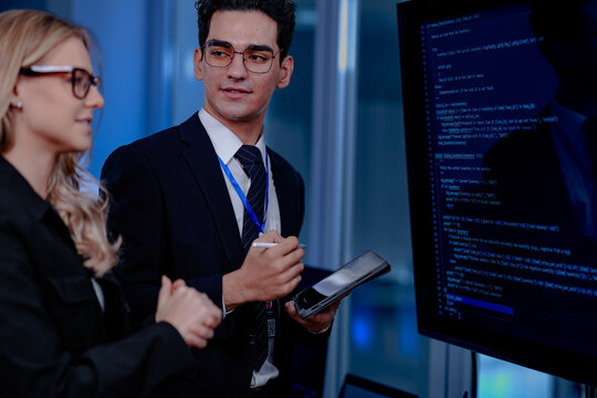 Code breakthrough achieved. Smiling senior developer points to a successful code segment on screen, sharing the solution with his colleague during a late night pair programming session.