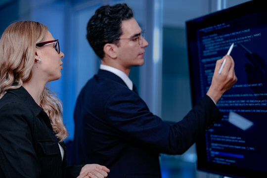 Code breakthrough achieved. Smiling senior developer points to a successful code segment on screen, sharing the solution with his colleague during a late night pair programming session.