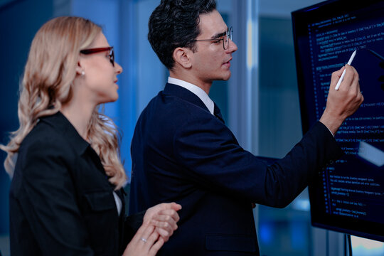 Code breakthrough achieved. Smiling senior developer points to a successful code segment on screen, sharing the solution with his colleague during a late night pair programming session.