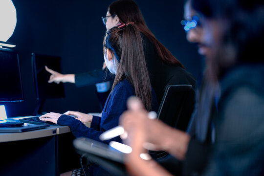 Focused female professionals collaborating late night in modern tech hub. Team members analyze data review designs pointing at screen typing notes on tablet intense project grind.