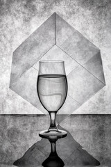Still life with a glass of liquid and a cube