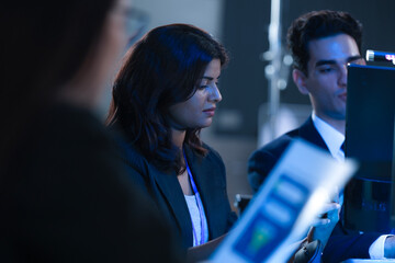 Monitoring AI training progress. Specialists oversee a machine learning model's training observing real time metrics on screen discussing adjustments via tablet interface late night.