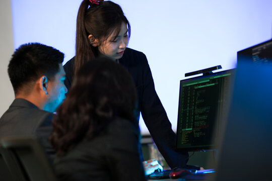 Knowledge transfer session late night. Experienced developer mentors junior colleagues explaining complex code logic pointing screen fostering growth skill development tech talent pipeline.