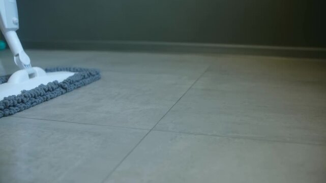 Modern spray mop with microfiber pad cleaning grey tiled floor in contemporary home. Housekeeping and domestic chores concept shows process washing room surface. Spray mop cleaning modern tile floor