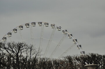 Views of a ferris wheel turning slowly against a cloudy sky in a city park during early evening