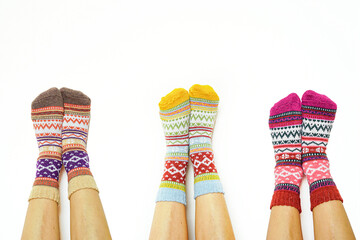 Three pairs of legs wearing colorful Fair Isle socks on a neutral white background. Symbolizes social comfort gathering, friendship bonding moment, shared cozy lifestyle, and winter season celebration