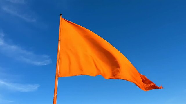 Orange nishan sahib flag waving beneath blue sky during gurpurab festival