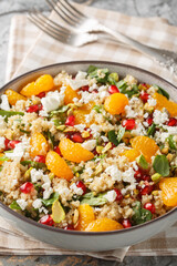 Quinoa salad with spinach, feta, tangerines, pomegranate, and pistachios, close-up in a bowl on the table. Vertical