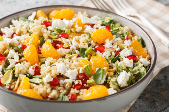 Diet quinoa salad with spinach, feta, tangerines, pomegranate, and pistachios dressed with a lemon-yogurt sauce, close-up in a bowl on a table. Horizontal - Powered by Adobe