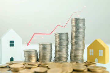 Stacks of coins with miniature houses and a downward red chart line representing real estate market decline, economic recession, housing price drop, and financial loss in property investment concept.