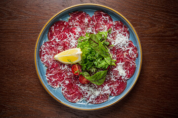 Beef carpaccio showcases vibrant red slices topped with cheese, served with greens and lemon