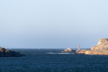 Rocky coastline on sunny day with lighthouse and open sea background in storm
