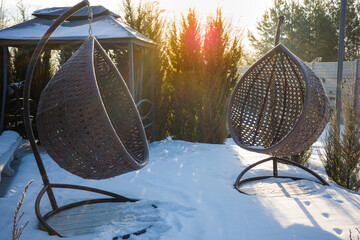 Hanging cocoon chair, rattan garden swing. View of the relaxation area near the house during the winter and frosty period.
