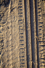 Intricate tire tracks pressed deep into warm, golden sand revealing textured patterns and casting long shadows under bright sunlight