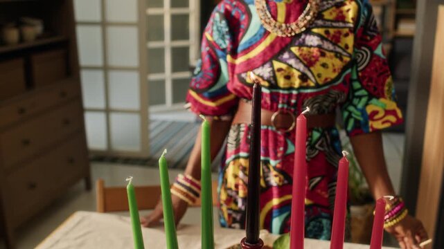 Midsection view of unrecognisable African American woman wearing colourful dress watching central Kwanzaa candle glowing in holder