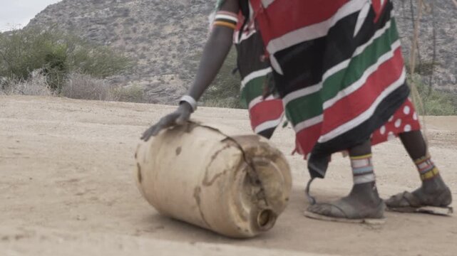 African women pushes a heavy water canister on the ground.