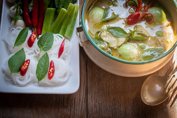 Authentic Thai green curry with tender chicken and eggplants served with rice noodles and fresh vegetables. Traditional Thai food still life on wooden table, beautifully arranged with basil leaves.