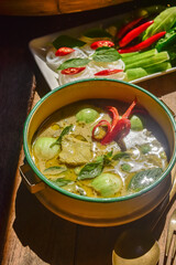 Authentic Thai green curry with tender chicken and eggplants served with rice noodles and fresh vegetables. Traditional Thai food still life on wooden table, beautifully arranged with basil leaves.