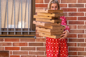 Blonde woman carrying pizza boxes in front of brick wall representing modern food delivery lifestyle and casual service