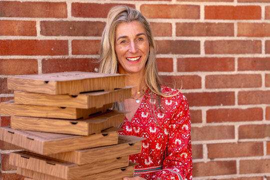 Cheerful blonde woman with pizza boxes standing near brick wall showing delivery service concept and modern fast food trend