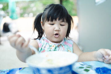 A cute little Asian girl is sitting on the dining table eating rice with relish,Cute asian kid girl...