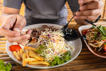 Close-up of human hand slicing steak on plate,Salad with meat on a plate, on a wooden table. Male hands with a fork and knife, cuts meat. close-up