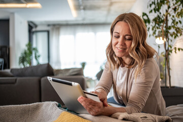 Smiling woman using digital tablet and credit card for online shopping at home