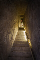 Dark corridor going downstairs, with staircase made of stone at the famous temple of Dendera, Egypt. Walls full of hieroglyphics at both sides. Vertical view with perspective.