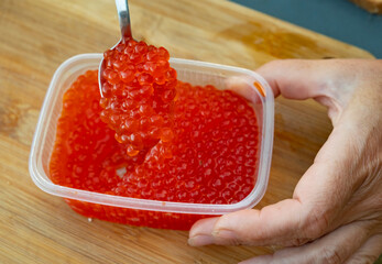 Bright red fish roe is carefully lifted with a spoon from a container during food preparation in a kitchen