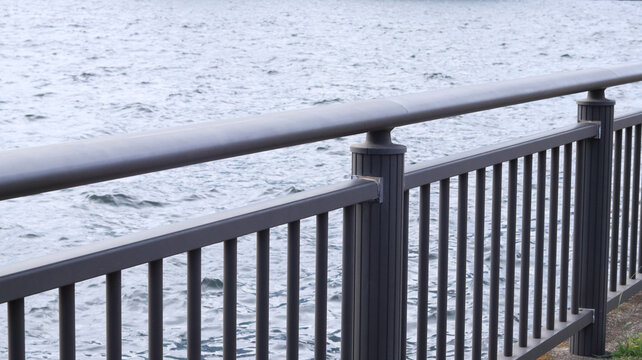 Modern metal railing by the waterfront with calm rippling water in the background.