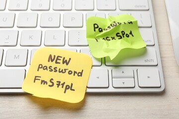 Changing password. Paper notes with new and old passwords and keyboard on light wooden table,...