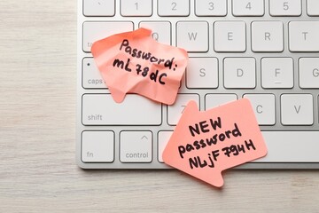 Changing password. Paper notes with new and old passwords and keyboard on light wooden table, top...