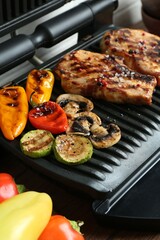 Electric grill with delicious vegetables and steaks on table, closeup