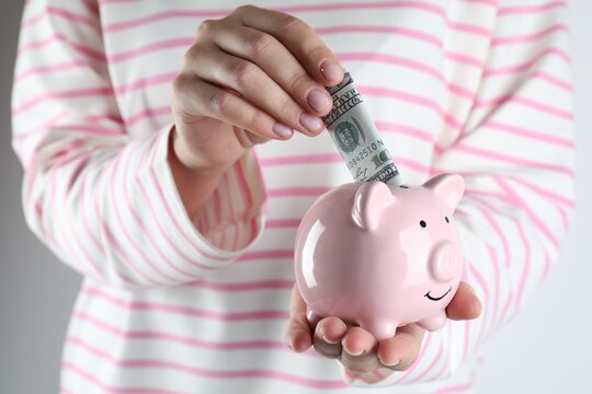 Saving money. Woman putting dollar banknotes into piggy bank on white background, closeup - Powered by Adobe
