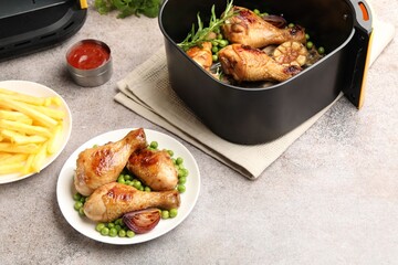 Air fryer with grilled chicken drumsticks and french fries on grey table, above view. Space for text