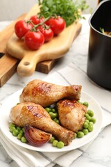 Grilled chicken drumsticks served with green peas on white marble table, closeup