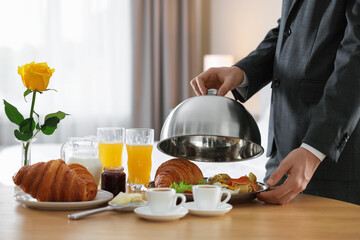 Waiter serving breakfast on wooden table in hotel room, closeup. Space for text