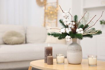 Winter composition with fir tree branches, cotton flowers in vase and burning candles on wooden table indoors, closeup. Space for text