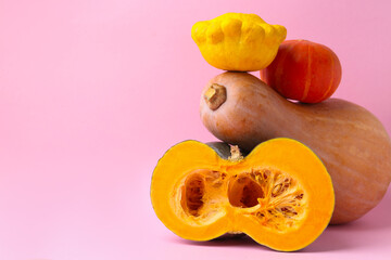 Whole, cut pumpkins and pattypan squash on pink background, closeup with space for text. Gourd family