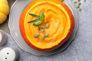Tasty pumpkin cream soup with seeds and basil served in pumpkin on grey table, flat lay