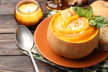 Tasty pumpkin cream soup with basil and croutons served in pumpkin on wooden table, closeup