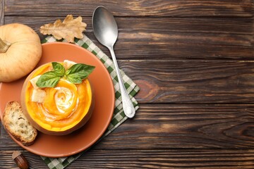 Tasty pumpkin cream soup with basil and croutons served in pumpkin on wooden table, flat lay. Space...