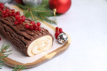 Delicious Yule log (traditional Christmas cake) with redcurrant, decor and fir tree branches on light table, closeup. Space for text