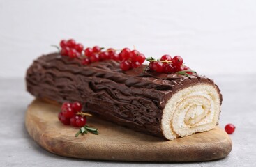Delicious Yule log (traditional Christmas cake) with redcurrant on light table, closeup