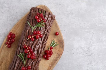 Delicious Yule log (traditional Christmas cake) with redcurrant on light table, top view. Space for text